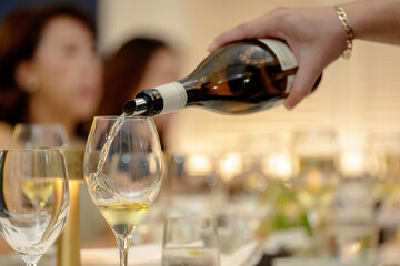 Close up of serving red and white wine in social setting. Close up hand pouring wine.