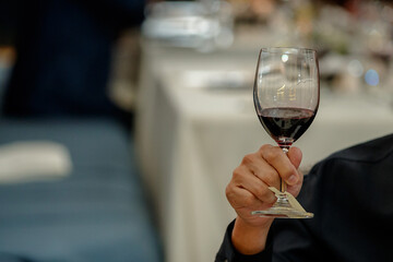 Hand holding a glass of red wine with blurry restaurant background