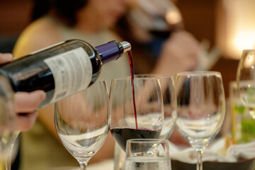 Close up of serving red and white wine in social setting. Close up hand pouring wine.