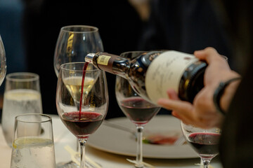 Close up of serving red and white wine in social setting. Close up hand pouring wine.