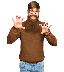 Young irish redhead man wearing casual clothes and glasses smiling funny doing claw gesture as cat,...