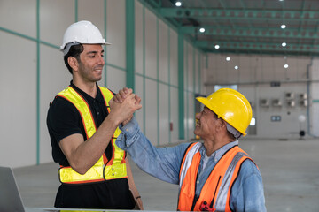 Technician and engineer discussing working together in warehouse.They are using laptop and shaking hands.