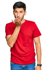 Young handsome man wearing casual red tshirt looking at the camera blowing a kiss with hand on air being lovely and sexy. love expression.