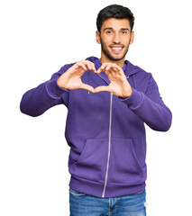 Young handsome man wearing casual sweatshirt smiling in love showing heart symbol and shape with...
