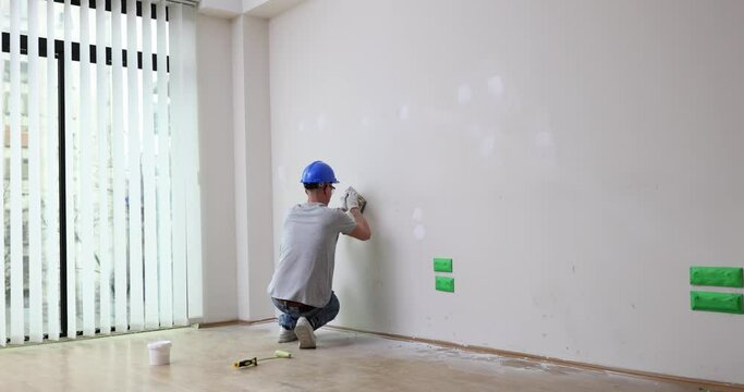 Man builder grinding wall with sandpaper. Surface preparation before painting, slowmotion