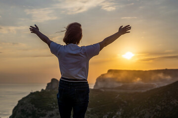 Happy woman on sunset in mountains. Woman standing with her back on the sunset in nature in summer...