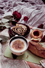 Breakfast in bed close-up, cappuccino in a light cup and pastries with poppy seeds on a board, against the background of a kitchen towel, a red rose and blanket