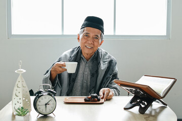 Elderly Asian muslim man sitting at dining table and drink a glass of water for break fasting in...
