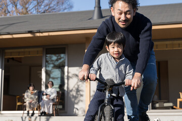 庭先で自転車の練習をする子どもを見守る父母　家族団欒の秋冬...