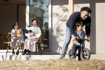 庭先で自転車の練習をする子どもを見守る父母　家族団欒の秋冬