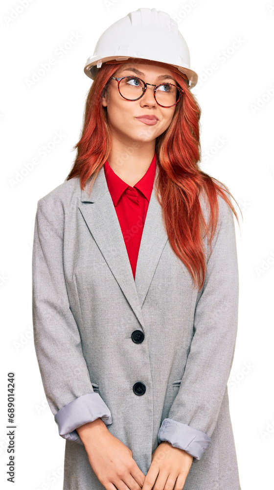 Wall mural young redhead woman wearing architect hardhat smiling looking to the side and staring away thinking.