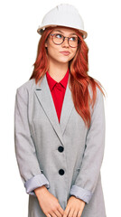 Young redhead woman wearing architect hardhat smiling looking to the side and staring away thinking.