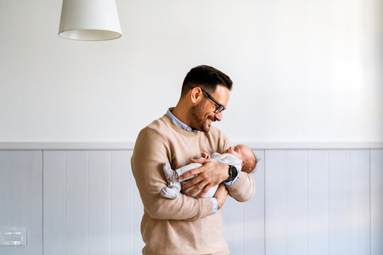 Portrait of a father hugging and kissing newborn baby. Authentic lifestyle touching tender moment.