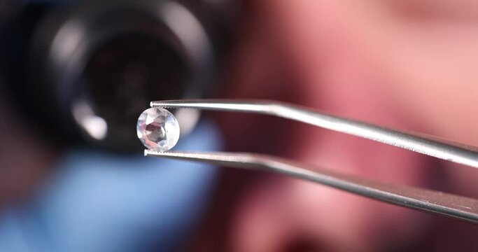 Jeweler holds precious transparent stone in tweezers. Difference between natural stone and artificial concept