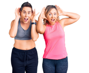 Couple of women wearing sportswear smiling cheerful playing peek a boo with hands showing face. surprised and exited