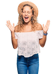 Beautiful caucasian woman wearing summer hat celebrating mad and crazy for success with arms raised...