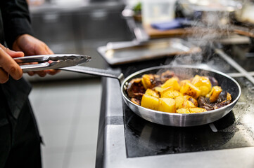 Chef cook hand cooking potato and meat food in pan at the restaurant kitchen