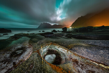 Overcast sky lit by Aurora Borealis over the famous rock formation, Dragon's Eye. Dramatic night scene at the Uttakleiv Beach, Lofoten Islands, Norway. - 689023201