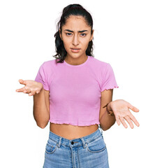 Hispanic teenager girl with dental braces wearing casual clothes clueless and confused with open...