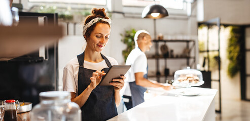 Waitress using digital tablet to view and manage orders in a coffee shop - obrazy, fototapety, plakaty