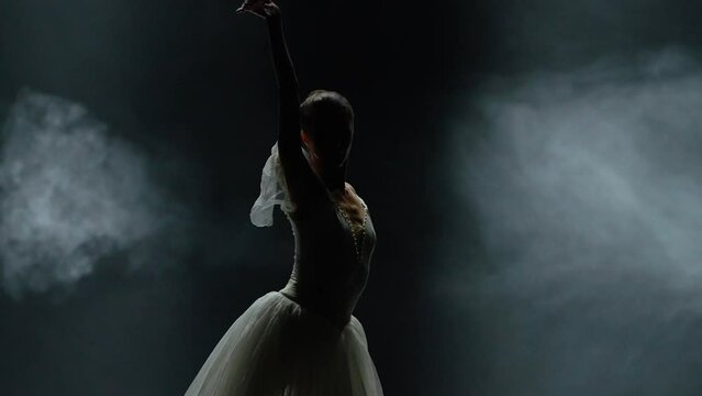 Ballet performance, dramatic dance, graceful ballerina in a white tutu, perform choreographic elements on a black background, haze effect on a dark stage.