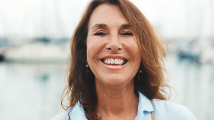 Close up, happy attractive middle age woman standing in port on yacht background looking at camera...