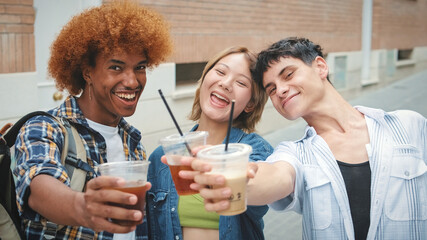 Group of friends looking at camera smiling, drinking takeaway drinks and raising toast