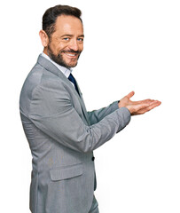 Middle age man wearing business clothes pointing aside with hands open palms showing copy space, presenting advertisement smiling excited happy