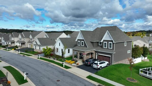 Suburban street with uniform houses, manicured lawns, and cloudy skies. Aerial shot of American flag waving on modern USA home.