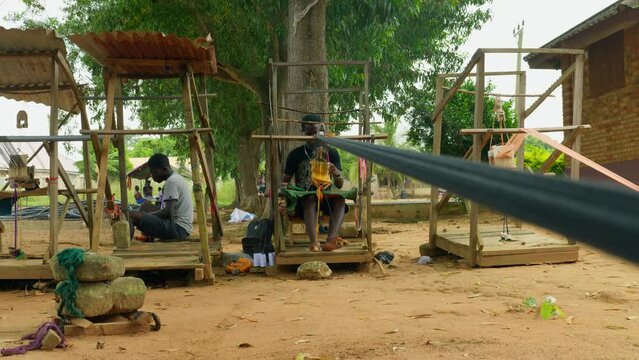 Happy African artisans from Ghana community manually weaving Kente textile