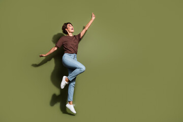 Full size photo of ecstatic woman dressed brown t-shirt pants flying catching object look empty space isolated on khaki color background - obrazy, fototapety, plakaty