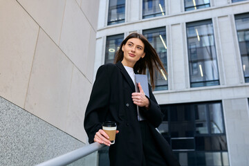 A female office employee is waiting for her colleague standing outside an office building before starting work