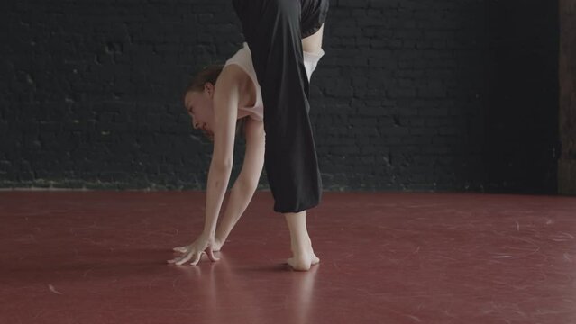 Full shot of young Caucasian woman dancing contemporary with acrobatic elements on parquet floor of dance studio with black loft style brick walls