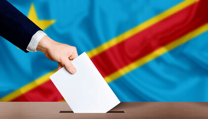 Hand holding ballot in voting ballot box with Democratic Republic of the Congo flag in background....