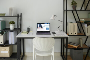 Opened laptop with financial services website on screen of desk of entrepreneur working from home
