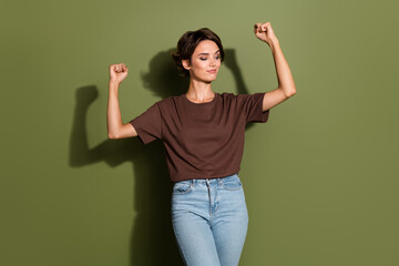 Photo of strong satisfied woman with bob hairstyle dressed t-shirt raising fists look at biceps isolated on khaki color background