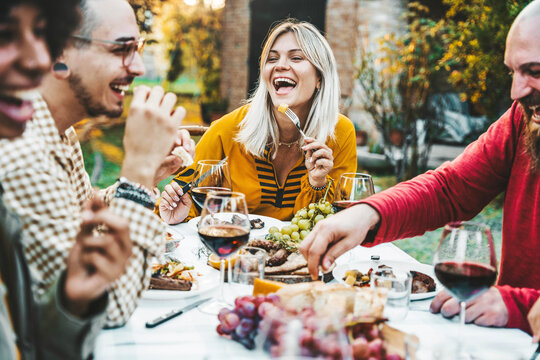 Happy friends having bbq dinner party in garden restaurant - Multiracial young people eating grill meat and drinking red wine in backyard - Food life style concept with guys and girls sitting outdoors