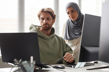 Portrait of IT team with Muslim young woman reviewing project and looking at computer screen