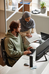 Vertical portrait of IT team of two people reviewing project together in office and using computers