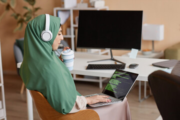 Side view portrait of Muslim young woman as female programmer writing code and wearing headscarf in...