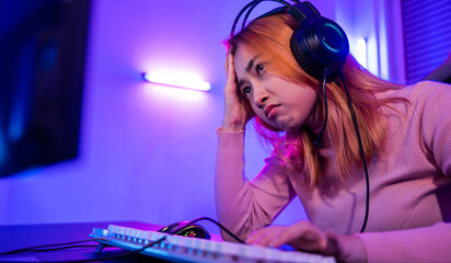 Game Over. Asian gamer playing online video game she losing and sad on computer PC colorful neon LED lights, young woman in gaming headphones feeling disappointed about lost game, E-Sport concept - obrazy, fototapety, plakaty