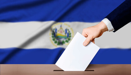 Hand holding ballot in voting ballot box with El Salvador flag in background. El Salvador...
