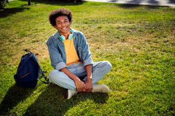 Photo of cheerful positive guy dressed jeans shirt headphones sitting green lawn outdoors urban city park