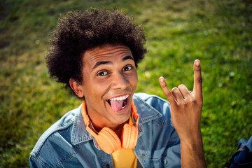 Photo of cool funky guy dressed jeans shirt headphones stick out showing hard rock sign outdoors...