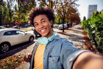 Photo of toothy funky guy dressed jeans shirt headphones tacking selfie smiling outdoors urban city...
