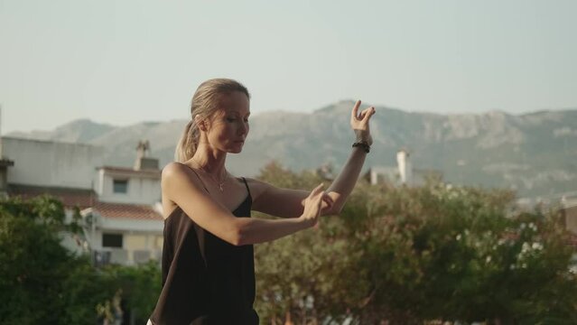 Oriental practice: a young woman does a qigong exercise against the backdrop of mountains. Master of oriental practices, qigong instructor. Concept of longevity, healthy body, balance.
