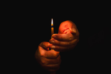 Burning candle in male hand, religion concept.Black background.Copy space.