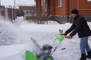 A man cleans snow in the winter in the courtyard of the house,  man cleaning snow with a snow blower