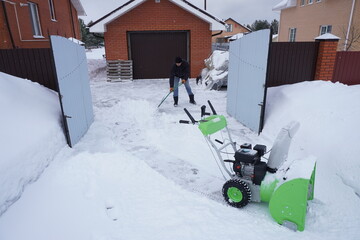 A man cleans snow in the winter in the courtyard of the house,  man cleaning snow with a snow blower