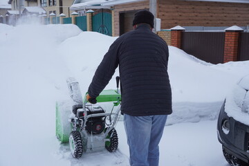 A man cleans snow in the winter in the courtyard of the house,  man cleaning snow with a snow blower